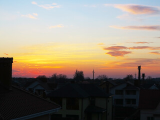 Dark, clear silhouettes of the roofs of houses with chimneys and pipes in the rays of the setting sun. Sunset in the city. Silhouette City landscape in the backlight of the sunset.