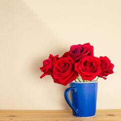 Red rose flowers in blue cup on wooden table with beige background. floral arrangement, copy space