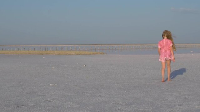 A girl walks through the snow, salty lake, in a summer afternoon in a red dress
