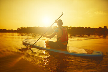 Silhouette of man paddling on paddle board at sunset. Water sport near the beach on sunset