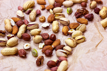 Different nuts: almonds, pistachios, peanuts, hazelnuts heap on light background.