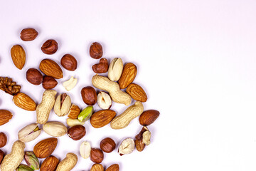 Top view of different nuts: almonds, pistachios, peanuts, hazelnuts mix heap on light background.