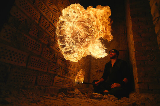 Male fakir blowing out fire in an abandoned building at night. Fire performer blowing out fire close-up.