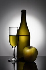 Stylish, modern still life with glass objects (a wine bottle and a wine glass) and an apple.