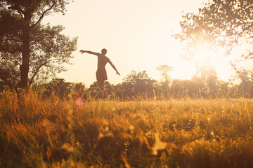 Fototapeta premium Young man walking on slackline in the meadow at sunset.