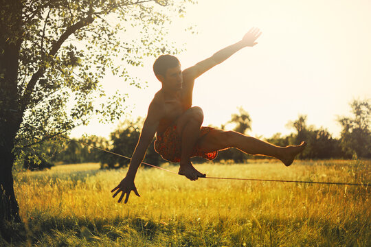 Young man walking on slackline in the meadow at sunset. - Powered by Adobe