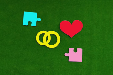 Puzzles in blue and pink, a pair of wedding rings, a red heart on a green background. Marriage, love, marriage registration. marriage contract.