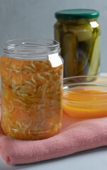 An open jar with fermented cabbage and carrots on a pink napkin in the foreground, pickled cucumbers in the background.