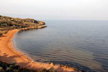 The seashore with rocks and a sandy bay, the day is sunny, the water in the sea is clear, the sky is clear and blue.