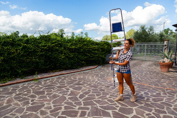 giovane donna di campagna con una camicia a quadri cammina con una scala in mano per andare a fare...