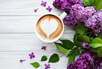 Obraz na płótnie Canvas Lilac and cup of coffee in flat style on white wooden background.