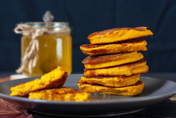 Pumpkin pancakes with honey on a plate. Dark brown and black background