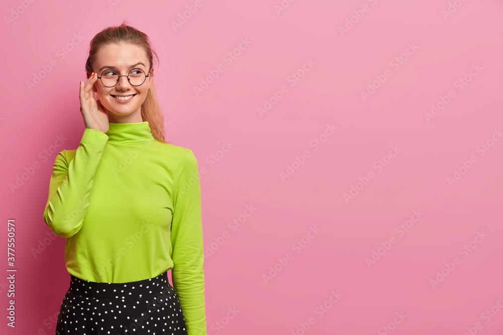 Wall mural horizontal shot of happy european girl has pony tail, wears green turtleneck and looks pleasantly as