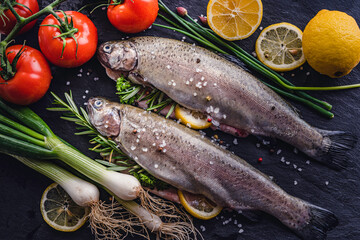fresh rainbow fish trout on black stone background with vegetables 