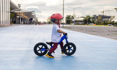 Adorable Asian kid boy (Toddler age 1-year-old), Wearing a Safety Helmet and Learning to Ride a Balance Bike in the Play Space.
