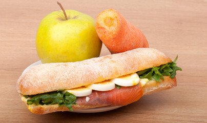 Real sandwich with smoked salmon, eggs and green with apple and carrot on a wooden background.
