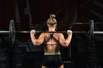 Fototapeta na wymiar Back view young adult girl doing barbell squats in gym. Woman with muscular body doing lifting exercise. Fit young female lifting barbells looking focused, working out in a gym fitness.