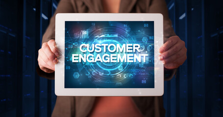 Young business person working on tablet and shows the inscription: CUSTOMER ENGAGEMENT, business concept