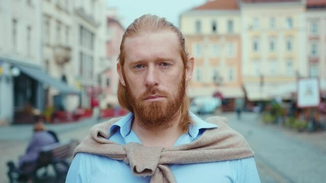 Portrait of confident ginger hipster bearded man in shirt standing on beautiful street city center looking straight into camera. Attractive redhead businessman.
