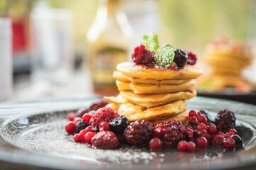 Delicious homemade pancakes with summer berries fruit for breakfast. Morning meal pancakes topped with honey on black dish.