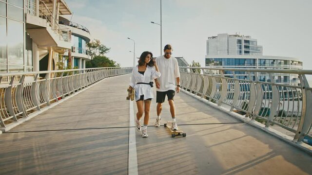 Millennial couple in love enjoying evening walk with skateboards