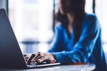 Black female in bright blue shirt typing on laptop keyboard - obrazy, fototapety, plakaty