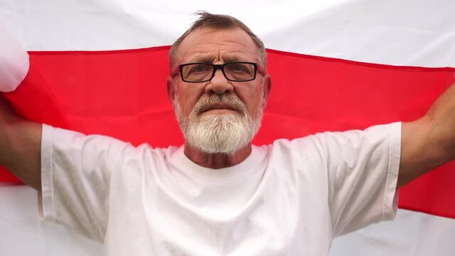 A man holds the flag of Belarus and stretches it with his arms in length against the background of the sky and the sun. Protest in Belarus