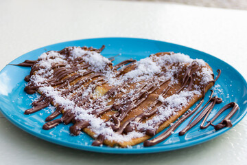 Romantic touch of heart shape pancake with chocolate cream and grated coconut on blue plate. Delicious sweet, original dessert concept