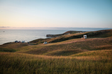camper vans and caravans on the top of the cliff under the Atlantic ocean, golden light through beautiful sunset in the North Spain, Cantabria, large meadow