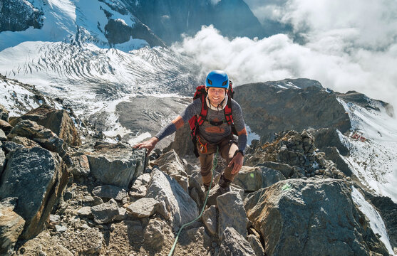 Climber in a safety harness, helmet with backpack asceding a rock wall with Bionnassay Glacier on background and looking at summit during Mont Blanc ascending, France route. Active climbing concept.