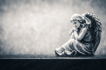 Angel figure sitting on an old headstone in a cemetery. Vintage, retro monochrome image with copy...