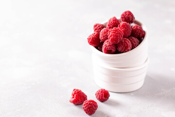 Fresh raspberries in white ceramic bowl on light background. Copy space.