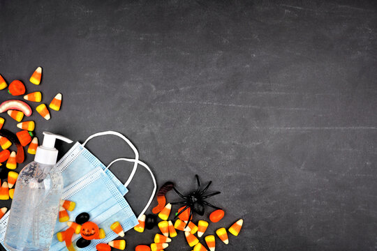 Halloween During Coronavirus Pandemic Concept. Above View Corner Border With Candy, Face Mask And Hand Sanitizer Over A Black Background.