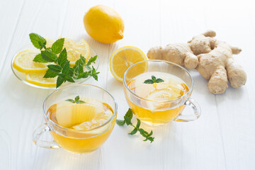 Two glass cups of healthy ginger tea with mint and lemon on white table