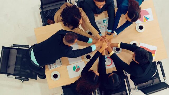 Happy business people celebrate teamwork success together with joy at office table shot from top view . Young businessman and businesswoman workers express cheerful victory showing unity and support .