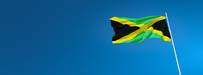 The beautiful flag of Jamaica waving against a blue sky in wide format. Jamaican national flag on background