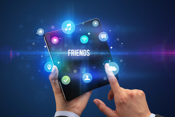 Businessman holding a foldable smartphone with FRIENDS inscription, social media concept