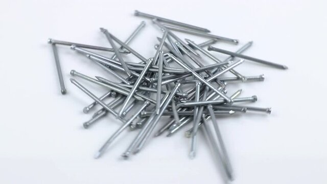 Close-up pile of grey metal nails rotating on white background, side view. Stainless fastener used in construction
