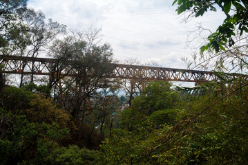 Train bridge in Guatemala City, made of steel, abandoned structure seen from urban forest area.