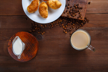 A mug of coffee with cream and a jug of cream and croissants on the table among the scattered coffee beans