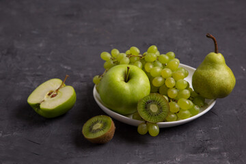 Fototapeta na wymiar still life of green fruits on a gray background. Apples, grapes, pears, kiwi