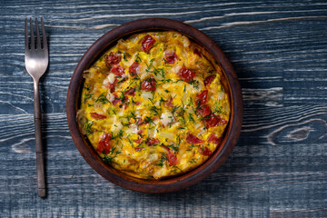 Ceramic bowl with vegetable frittata, simple vegetarian food. Frittata with tomato, pepper, onion and cheese on wooden table, close up