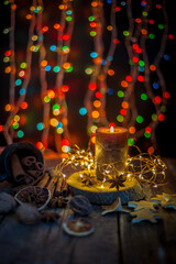 Good New Year spirit. Candle, garland, Christmas lights. Spices are anise star, an orange peel on a wooden table. Still life, cozy Christmas mood.