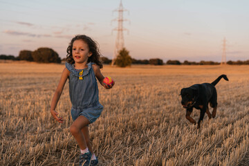 Young girl playing with her dog in the field during sunset