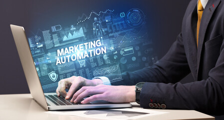 Businessman working on laptop with MARKETING AUTOMATION inscription, cyber technology concept