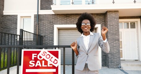 Happy young African American beautiful female real-estate agent dancing and having fun at suburb...