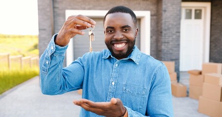 Portrait of cheerful happy African American man smiling to camera and showing key to camera while...