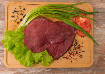raw beef meat with vegetables on wooden plate.