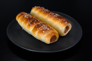 Sausage in the dough baked. Fast food photo subject on a black background.
