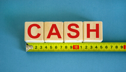 'Cash' word on cubes arranged behind the ruler on beautiful blue background. Concept.